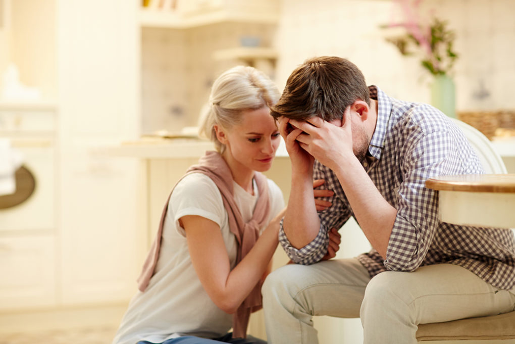Young woman comforting her unhappy and desperate husband after saying bad news