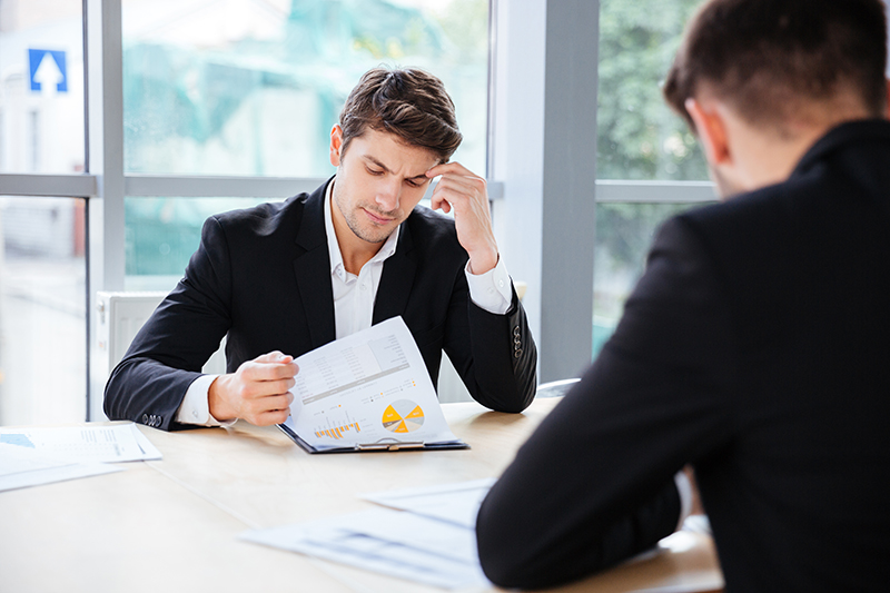 Two thoughtful young businessmen working with business plan in office