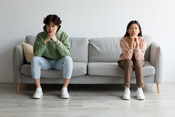 Family conflict, divorce, breakup concept. Stubborn young Asian couple sitting on opposite sides of couch in silence after fight, indoors. Offended millennial man and woman ignoring one another