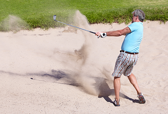 Playing out of a tough bunker. Action shot of a mature man playing a shot from a sand bunker